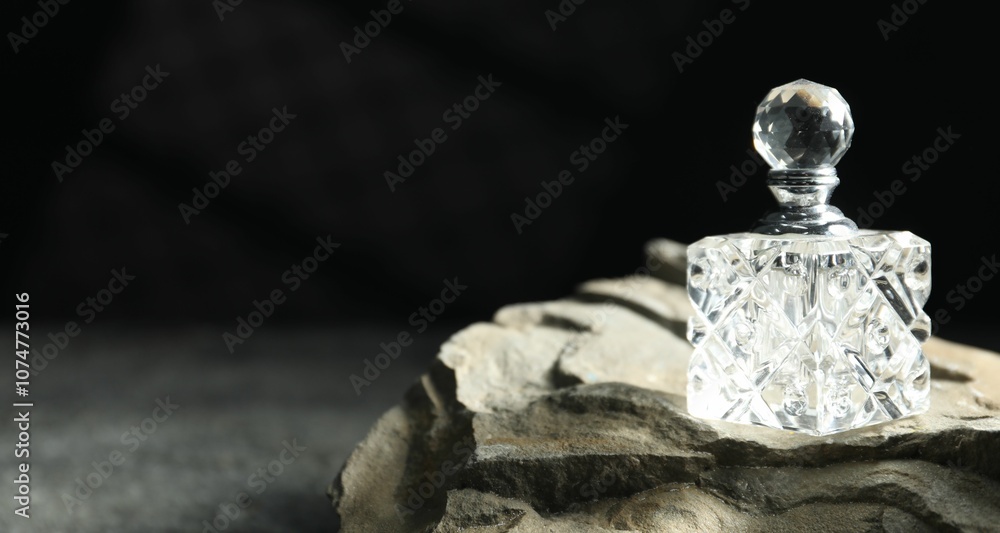 Fototapeta premium Bottle of fragrant perfume and rock on grey table, space for text