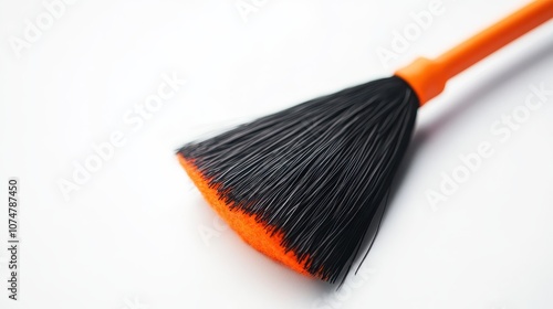 A close-up of a broom with a bright orange handle and black bristles, angled against a softly lit white background. Ideal for home care, cleaning supplies, or DIY promotions.