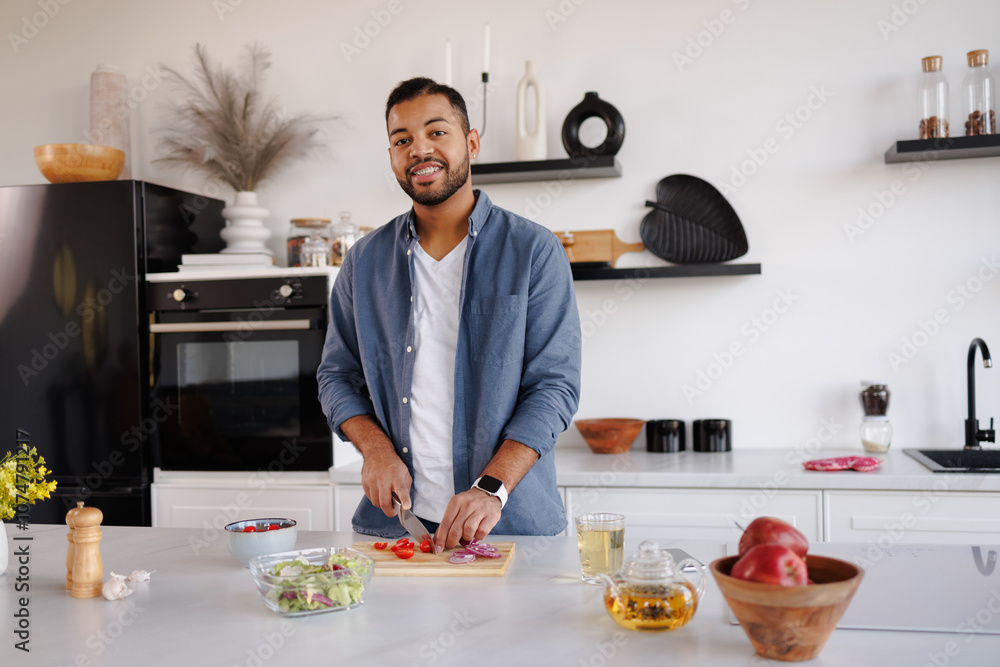 Smiling african american man looking at camera while cooking fresh salad in kitchen at home Smiling african american man looking at camera while cooking fresh salad in kitchen at home