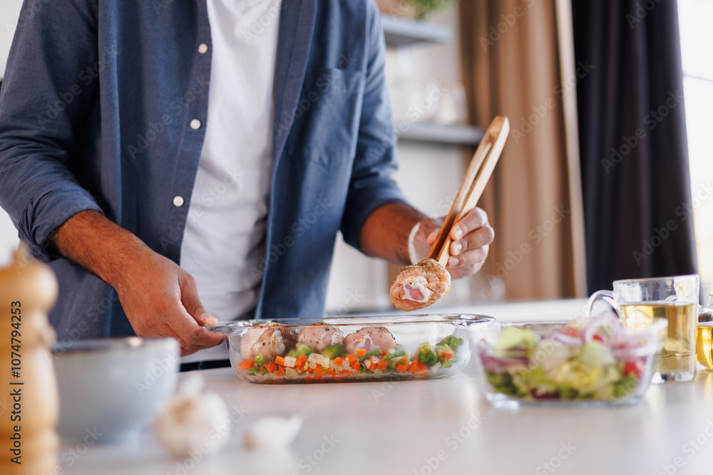 Partial view of african american man putting raw chicken legs in baking dish near tea and salad in kitchen Partial view of african american man putting raw chicken legs in baking dish near tea and salad in kitchen