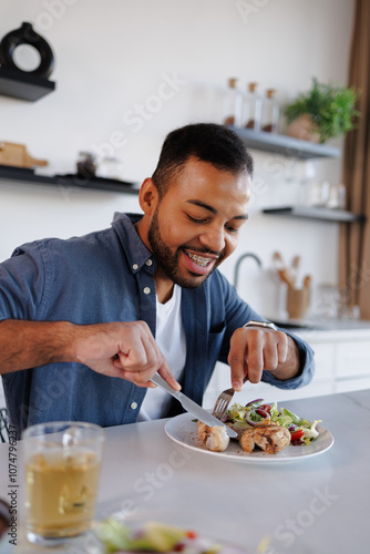 Smiling african american man eating chicken legs and fresh salad near herbal tea at home