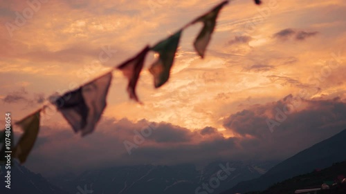 4K shot of defocused prayer flags waving in front of snowy Himalayan mountain range during the sunset as seen from Khangsar village in Lahaul and Spiti district, Himachal Pradesh, India.