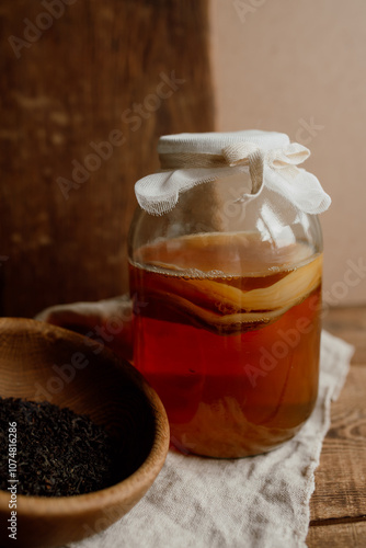 Glass jar with kombucha drink and wooden bowl with tea. Kombucha tea and ingredients