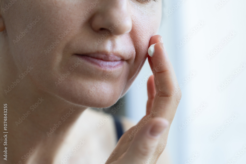 Obraz premium Woman applying anti agin cream on wrinkles on her face. Closeup. Skin care.