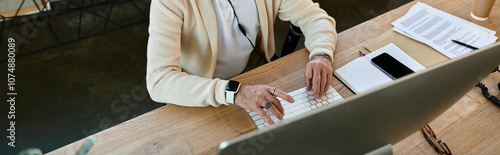 A stylish senior businessman focuses on his work, typing on a sleek keyboard in a contemporary office.