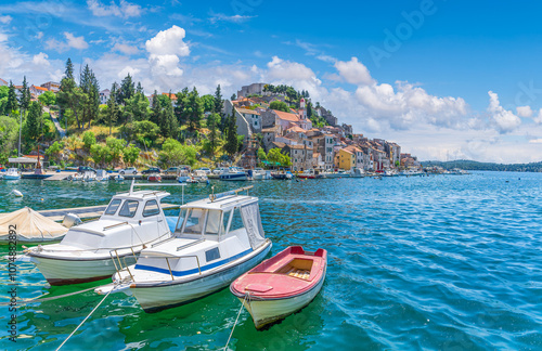 Fototapeta Naklejka Na Ścianę i Meble -  Serene harbor of Sibenik, Croatia, featuring boats docked along the Adriatic coast, historic buildings, and clear blue waters on a sunny day.