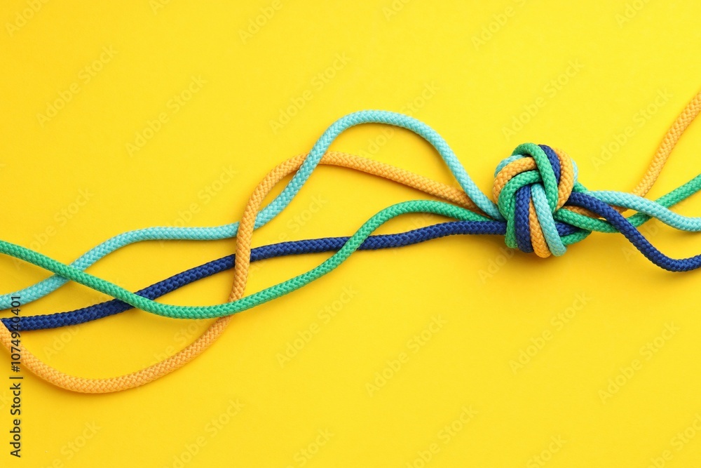Colorful ropes tied in knot on yellow background, top view. Unity concept Colorful ropes tied in knot on yellow background, top view. Unity concept