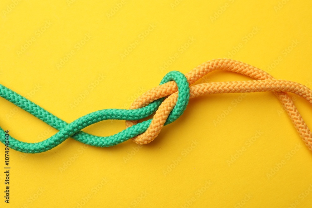 Obraz premium Colorful ropes tied in knot on yellow background, top view. Unity concept