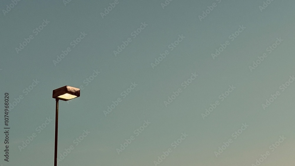 A single light pole with a lit lamp against a clear, cloudless sky, giving a simple and serene feel. A single light pole with a lit lamp against a clear, cloudless sky, giving a simple and serene feel.