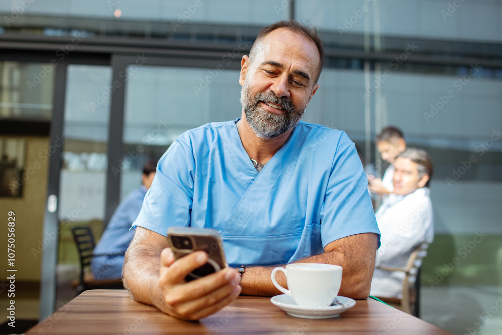Male doctor enjoying coffee while checking phone outdoors Male doctor enjoying coffee while checking phone outdoors