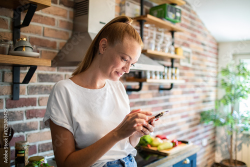 Young woman holding smartphone in modern kitchen