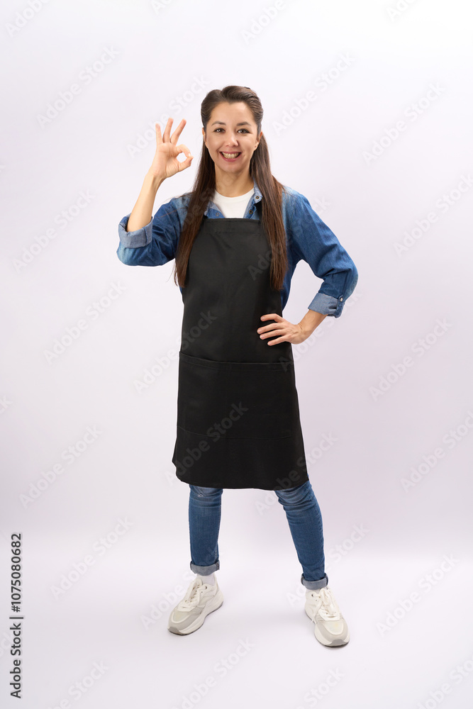 Full length portrait of a female chef showing ok sign, wearing black apron and standing against, white background, vertical Full length portrait of a female chef showing ok sign, wearing black apron and standing against, white background, vertical