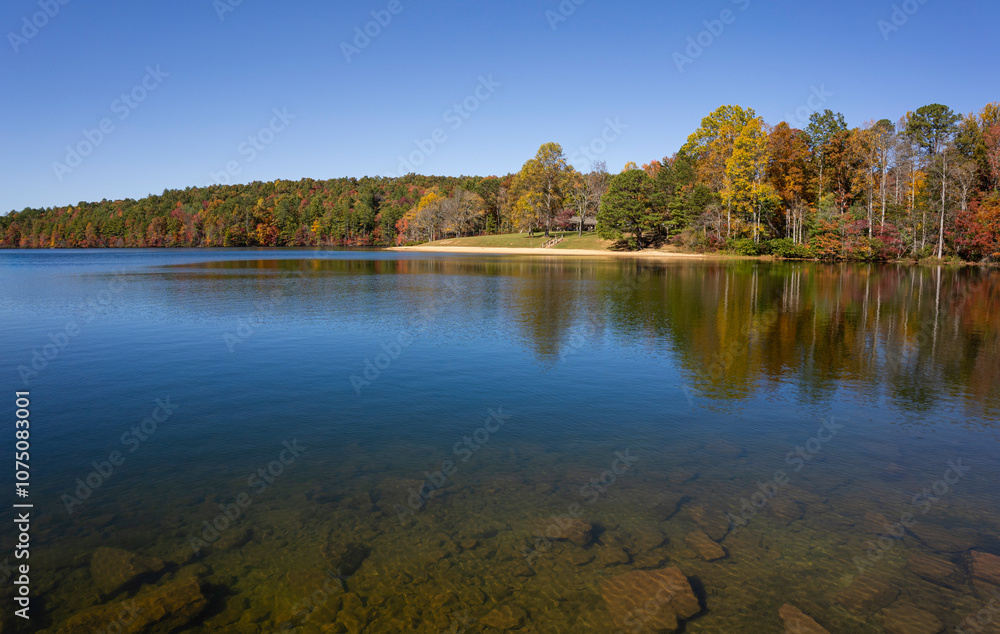Fototapeta premium Indian Boundary Lake in autumn, vibrant red, yellow, and green trees reflect in the calm blue water and a lakeside swimming area visible. Accessed from the Cherohala Skyway in Tennessee. Horizontal