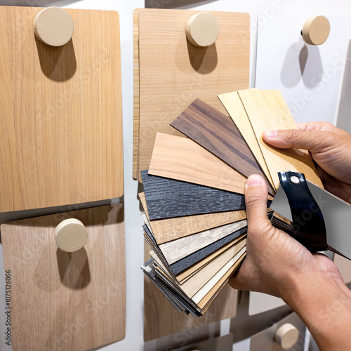 Designer hand picking sample of wood laminated from natural collection in material showroom. Choosing wooden veneer texture or set of MDF board swatch fan for interior finishing or furniture design