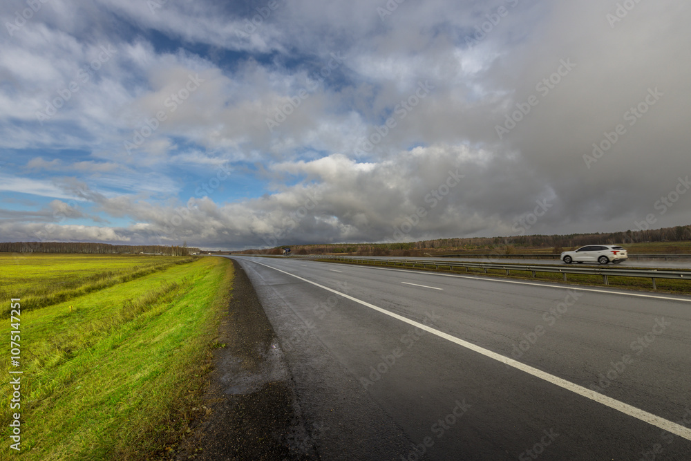 A car is driving down a road with a cloudy sky in the background A car is driving down a road with a cloudy sky in the background