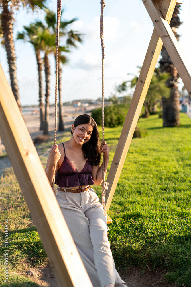 Beautiful young woman relaxing on a swing in a park near the beach Beautiful young woman relaxing on a swing in a park near the beach