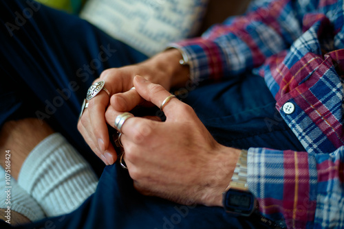 Close-up of a man with clasped hands wearing silver rings, checkered shirt, white socks and jeans. photo