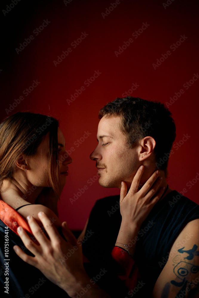 A couple engages in an intimate moment, facing each other closely with expressions of affection on a red background. A couple engages in an intimate moment, facing each other closely with expressions of affection on a red background.