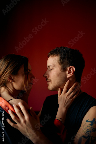 A couple engages in an intimate moment, facing each other closely with expressions of affection on a red background. photo