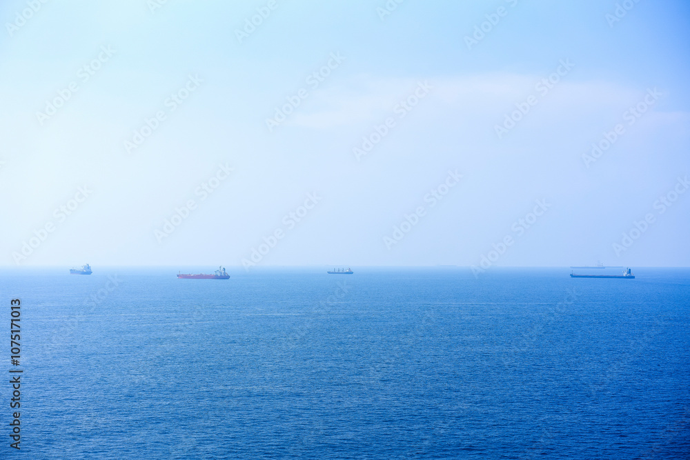 Calm blue sea with mist and multiple cargo ships on the horizon under a clear sky, South China Sea Calm blue sea with mist and multiple cargo ships on the horizon under a clear sky, South China Sea