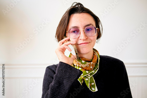 Woman with glasses smiling while holding her smartphone to her ear photo