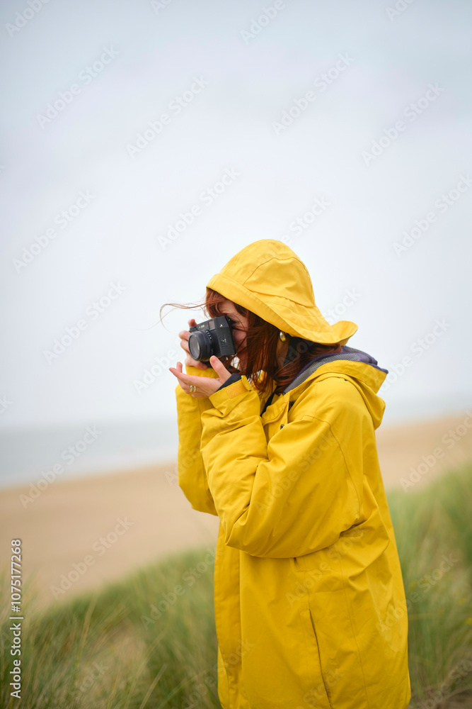A photographer in a yellow raincoat takes a photo on a beach with overcast skies, Belgium A photographer in a yellow raincoat takes a photo on a beach with overcast skies, Belgium