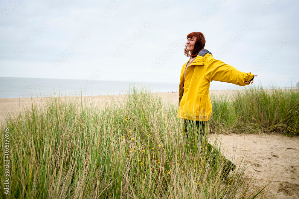 Woman in a yellow raincoat enjoying the calm at a beach with tall grass, Belgium Woman in a yellow raincoat enjoying the calm at a beach with tall grass, Belgium