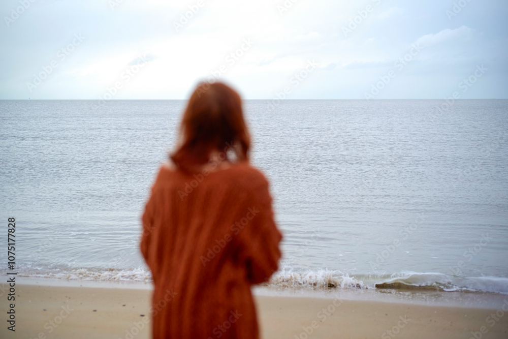 Blurry woman in a cozy sweater gazing at the serene ocean from a sandy beach, Belgium Blurry woman in a cozy sweater gazing at the serene ocean from a sandy beach, Belgium