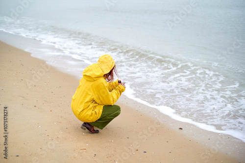 Person in a yellow raincoat crouches on a sandy beach looking at the sea, Belgium photo