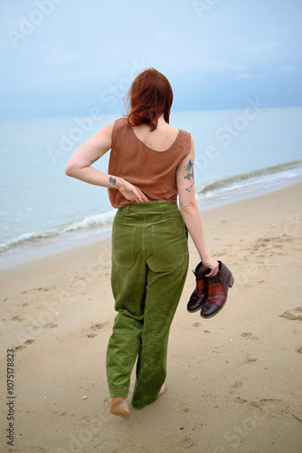 Woman with tattoos walks barefoot on a sandy beach holding her shoes in her hand, Belgium photo