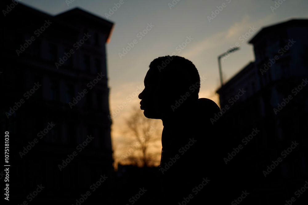Silhouette of a young man's profile against a twilight sky with blurred buildings in the background, Berlin, Germany Silhouette of a young man's profile against a twilight sky with blurred buildings in the background, Berlin, Germany
