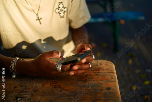 Close-up of a young man's hands holding a smartphone at a wooden table with sunlight casting warm tones, Berlin, Germany photo