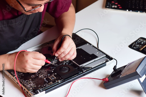 Computer technician wearing glasses A laptop motherboard repairman is using an IC meter to find faults on the motherboard to repair on his table. Board repair using modern technology