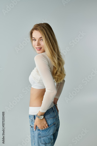 A beautiful young woman smiles playfully while wearing a stylish outfit, showcasing her confidence.