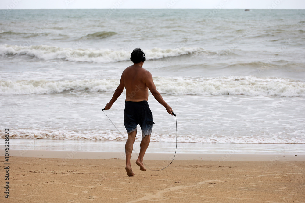 Training on the beach, man jumps with skipping rope on sea waves background. Exercise on a nature Training on the beach, man jumps with skipping rope on sea waves background. Exercise on a nature