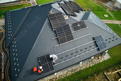 Builders building photovoltaic solar module station on roof of house. Men electricians in helmets installing solar panel system outdoors. Concept of alternative and renewable energy. Aerial view.