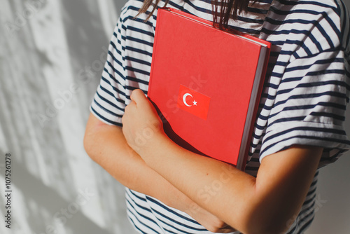 One child girl, whose face is not visible holds a red turkish language textbook with Turkey flag, foreign language learning concept photo