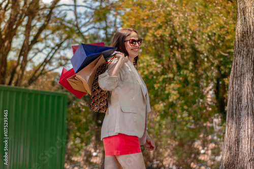 portrait of 50 year old woman walking in the park smiling and holding shopping bags
