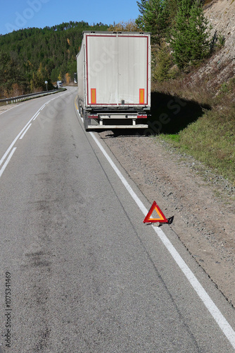 broken truck is standing on the side of the road. A red emergency stop sign stands on the road in front of the broken car.