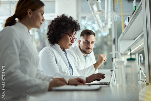 Team of biotechnologists cooperating while reading scientific data on a computer in laboratory.