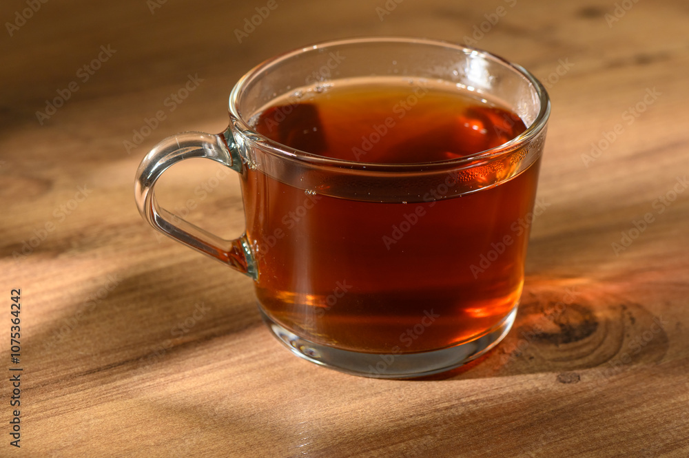 Warm cup of freshly brewed herbal tea resting on a rustic wooden table in soft afternoon light Warm cup of freshly brewed herbal tea resting on a rustic wooden table in soft afternoon light