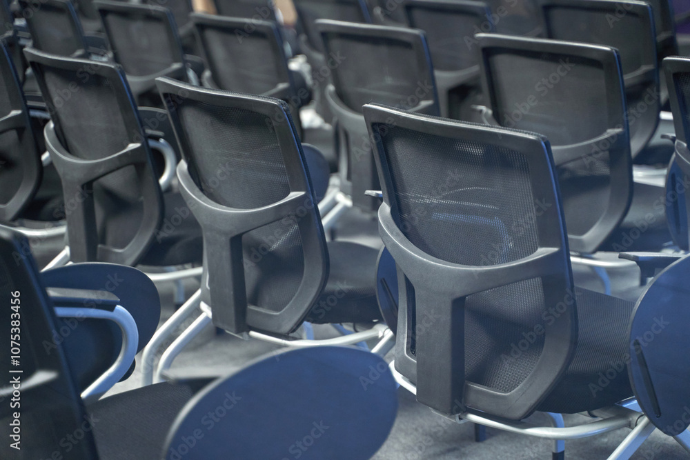 Empty conference room with rows of modern black office chairs arranged in neat alignment at corporate meeting venue Empty conference room with rows of modern black office chairs arranged in neat alignment at corporate meeting venue