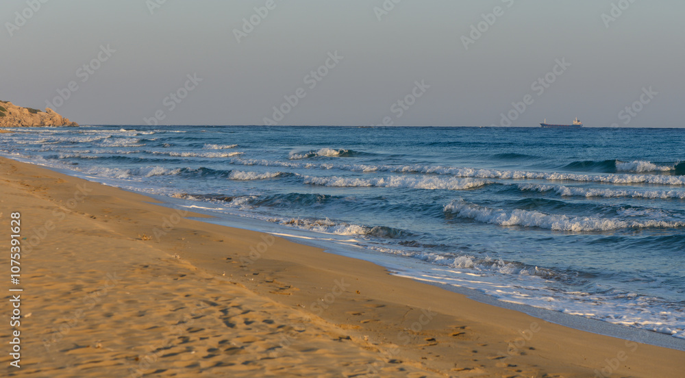 Waves gently lap at the sandy shore under a tranquil sky during sunset near an ocean coastline. Waves gently lap at the sandy shore under a tranquil sky during sunset near an ocean coastline.