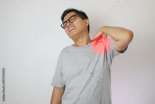 Adult Asian man touching his left shoulder with pain expression. photo