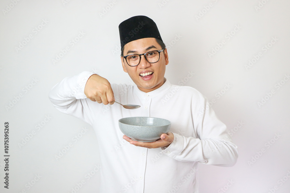 Excited young Asian Muslim man wearing Arabic clothes standing while holding bowl and saying yes it's time to break fast isolated on white background. People religious Islamic lifestyle concept. Excited young Asian Muslim man wearing Arabic clothes standing while holding bowl and saying yes it's time to break fast isolated on white background. People religious Islamic lifestyle concept.