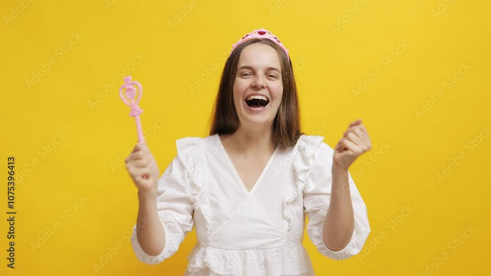 Excited woman celebrating with a magic wand in front of a yellow background Excited woman celebrating with a magic wand in front of a yellow background