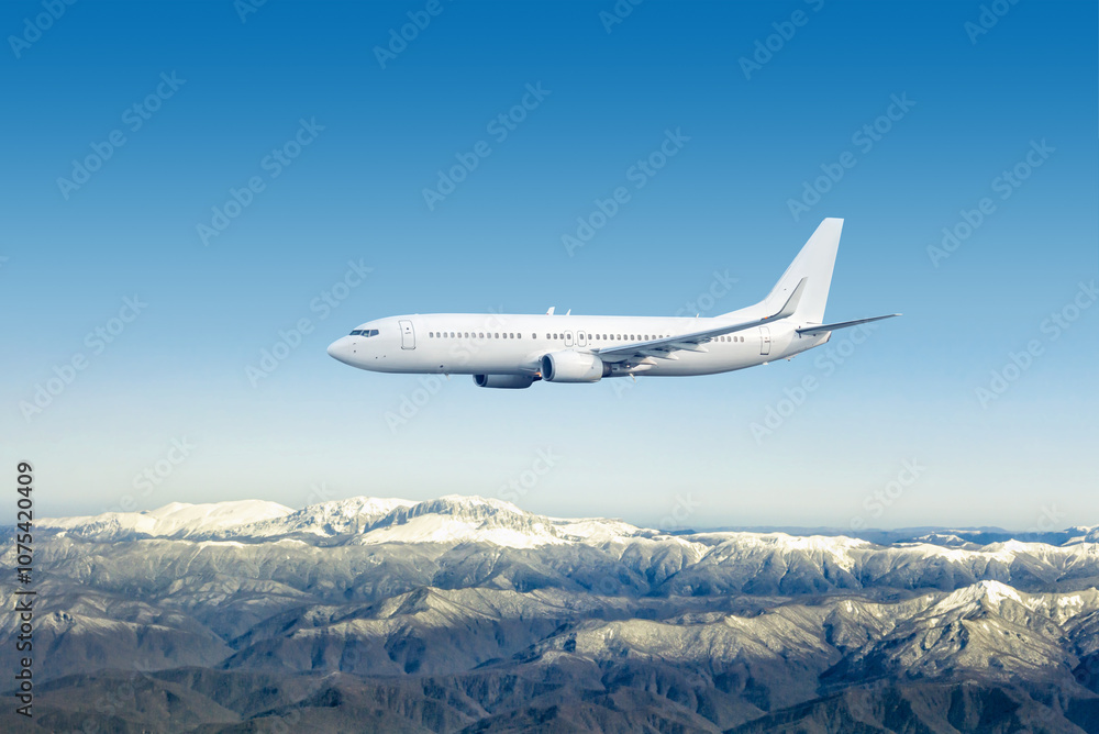 Fototapeta premium White passenger plane flies over snow covered mountains