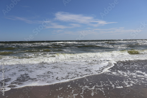 Waves Crashing on Sandy Shoreline Under Clear Blue Sky