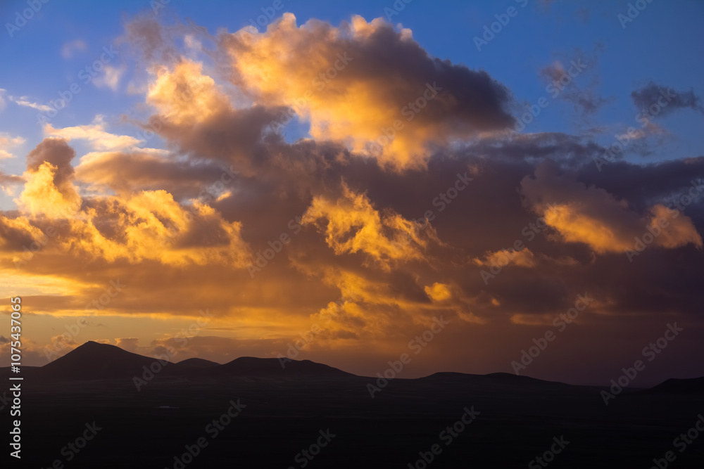 Sunset Over Lanzarote Island with Volcanic Peaks Silhouetted Against Vibrant Orange Clouds. Canary Islands, Spain. Sunset Over Lanzarote Island with Volcanic Peaks Silhouetted Against Vibrant Orange Clouds. Canary Islands, Spain.