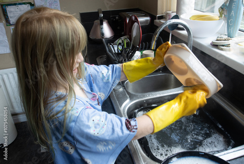Obraz na płótnie Child (8-9 years old) in Yellow marigold gloves washing up inside kitchen during day cleaning cat bowl w salonie